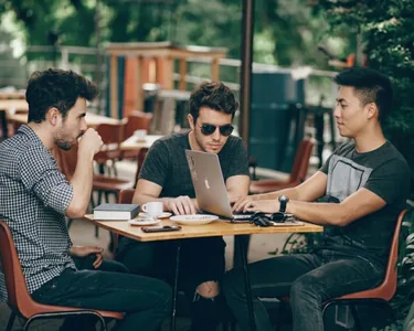 Three teammates reviewing work on a laptop at an outdoor café table.